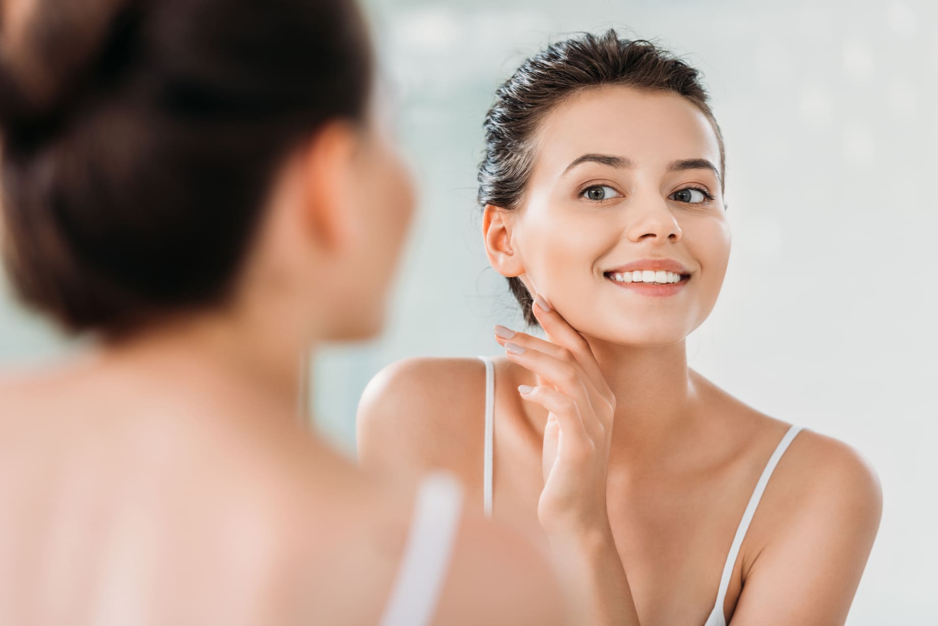 woman in front of glass looking at her skin