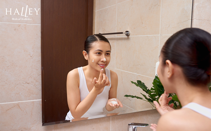 Woman washing her face in the mirror as part of skincare routine.