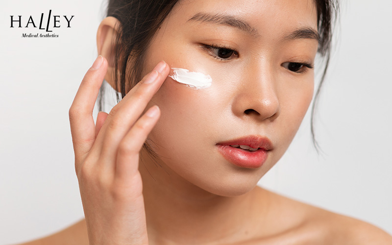 A woman applying moisturizer to her cheek for skin hydration.